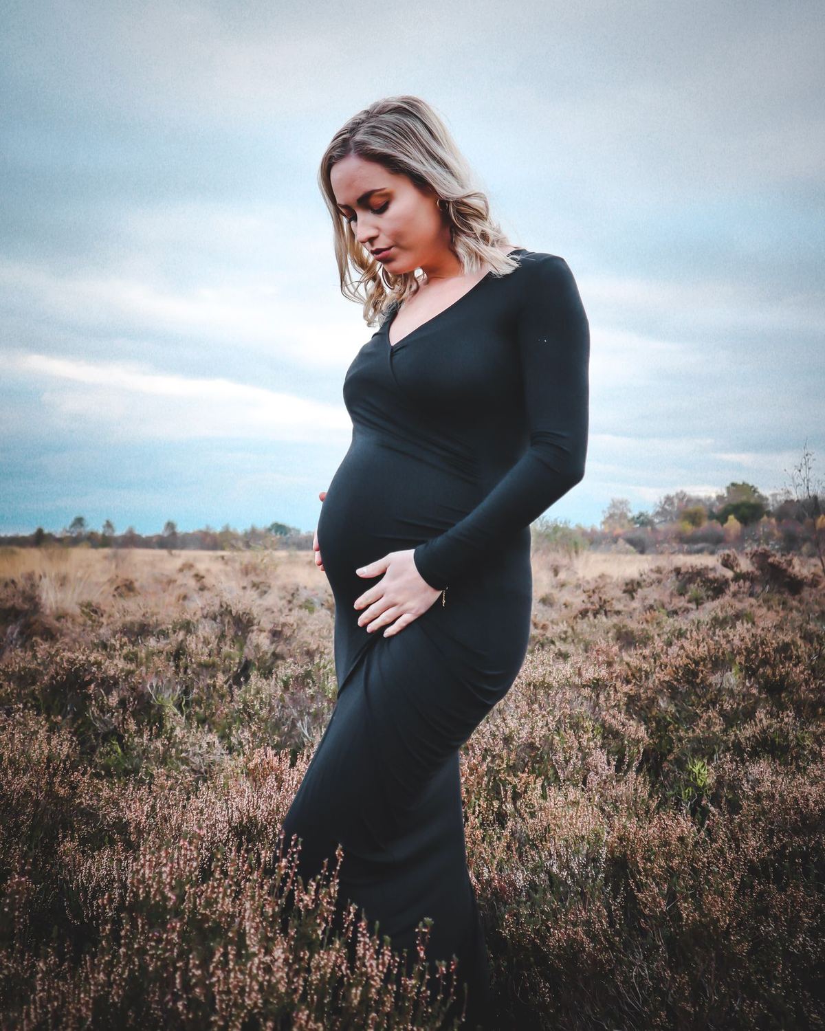 Gestante de vestido escuro em pé num campo aberto