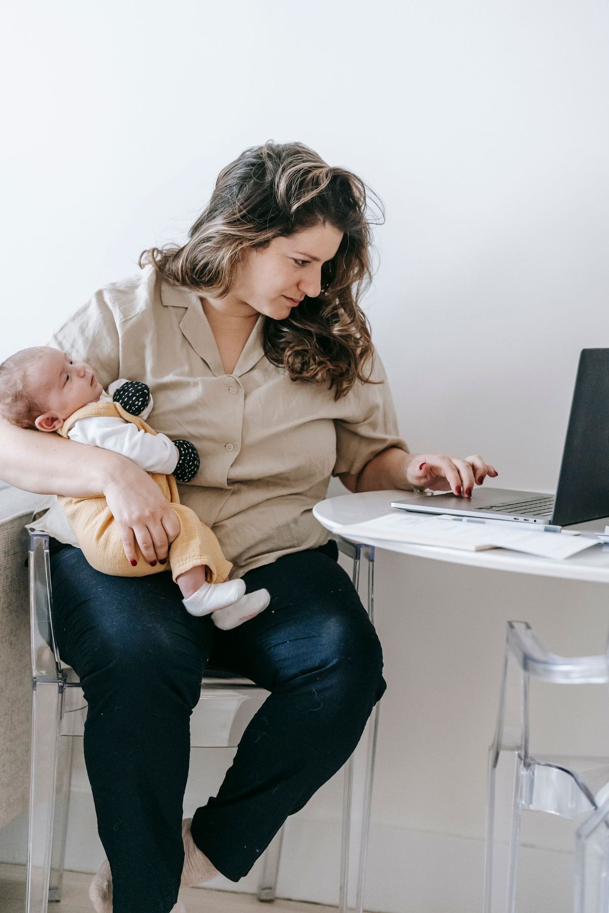Mãe com o bebê no colo usando um notebook sobre a mesa