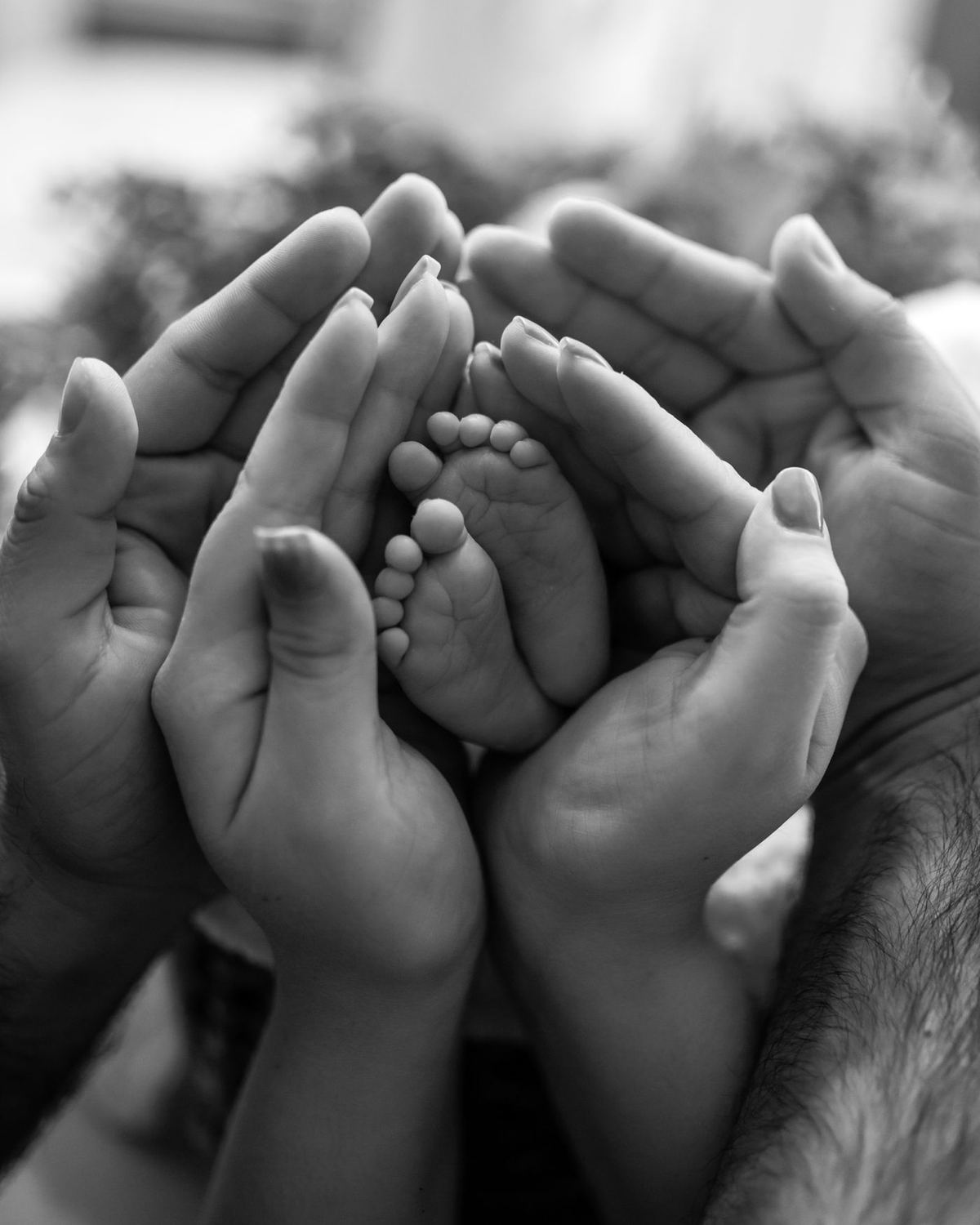 Mãos de adultos em volta dos pés de um recém-nascido